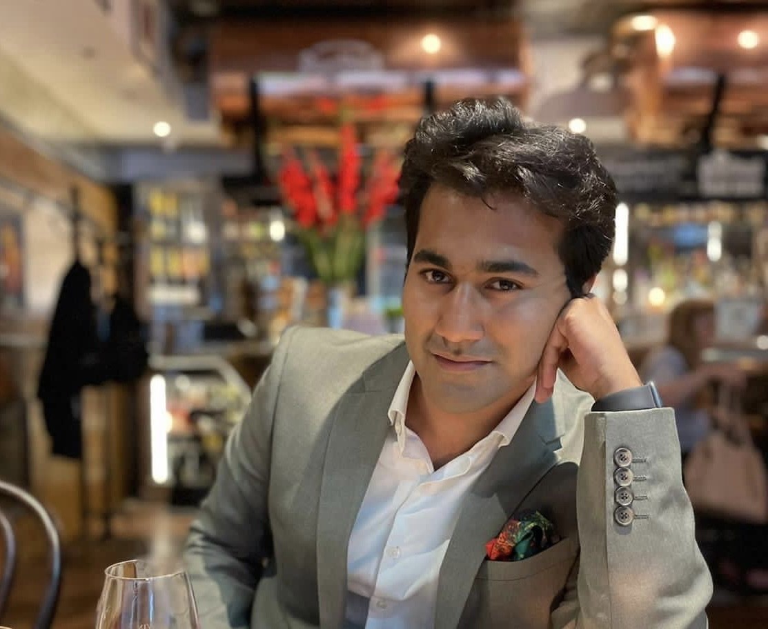Utkarsh Amitabh rests his arm on a table and looks directly at the camera, at a restaurant.
