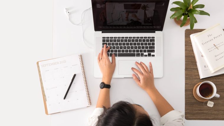 a birds eye shot of a girl working at her desk with a laptop, books and a mug of coffee