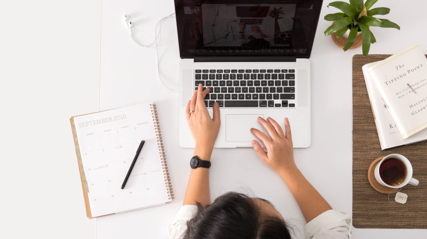 a birds eye shot of a girl working at her desk with a laptop, books and a mug of coffee