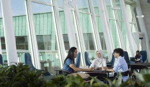 Three students sit at a table in a bright lounge in the University of Lancaster.