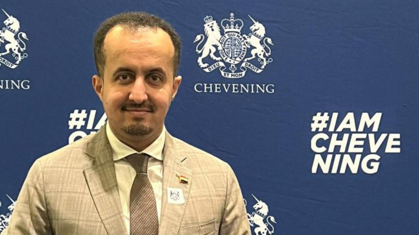 Hamzah standing in front of a Chevening sign