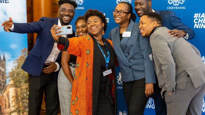 Chevening Scholars taking a selfie in front of a Chevening banner at the 2024 Chevening conference.
