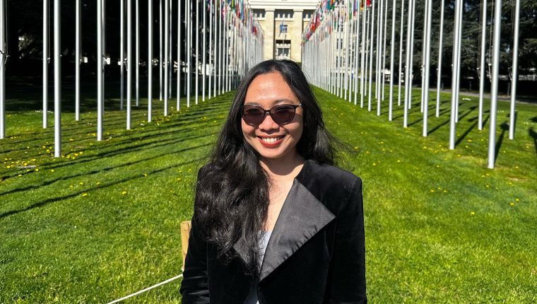 A woman standing with flags behind her on a sunny day in a field.