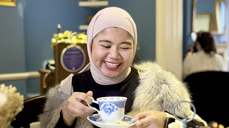 A woman is holding a tea cup that is decorated with blue and white patterning, typical of the regency era.