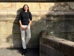 Nora leaning against an old looking building, smiling at the camera.