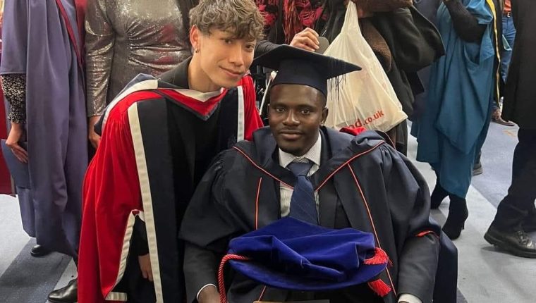 Graduates wearing gown and caps smile with friends and family around.