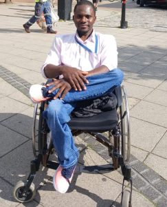 Mahmud sits in a wheelchair with his legs crossed, smiling at the camera.