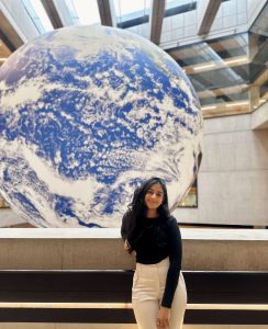 Scholar stands in front of a large blue and white globe.