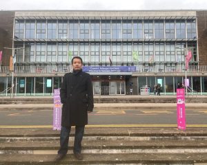 Scholar stands on the steps in front of a large Swansea University building.