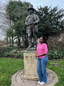 Scholar stands next to a statue of a male figure.