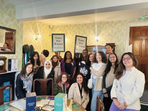 Women standing in a group shot with a sign that says votes for women