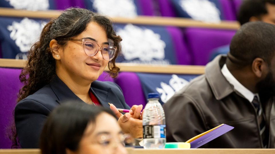 A woman clapping and looking into the distance. Behind her are Chevening branded tote bags.